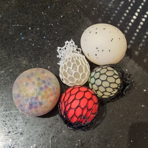 2 Stressbollar + 3 Stressbollar med Nät - Bilderna visar flera olika stressbollar i olika färger och former, vissa med nät runt sig som ger en unik känsla när de kläms. Perfekta för att slappna av, minska stress eller bara ha kul! Passar både ungdomar och unga vuxna som vill ha något att pilla med under plugg eller gaming. Vill dock påpeka att stressbollen med vitt nät runt sig inte är riktigt lika bra som de andra två, men allt annat är i bra skick💓