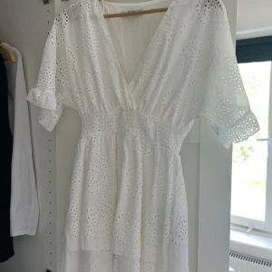 Vit broderad sommarklänning från Amisu - Superfin vit klänning från Amisu med broderade hålmönster, v-ringning och smock i midjan. Klänningen har korta ärmar och volangig kjol, perfekt för varma dagar. Söt och luftig stil som känns riktigt fräsch. Använd en gång. Har lite orangea fläckar längst fram men går bort i tvätten
