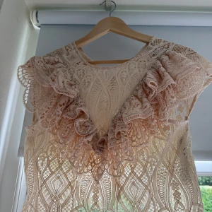 Beige spetsblus med volangdetaljer - Superfin beige blus från Zara. Blusen har ett genombrutet mönster och är ärmlös, perfekt för dig som gillar romantisk och bohemisk stil. Snygg att styla med jeans eller kjol för en trendig look.