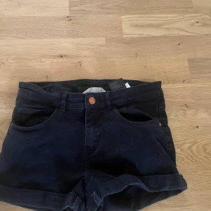 Svarta jeansshorts från H&M - Svarta jeansshorts från H&M med klassisk femficksdesign och uppvikta benslut. Modellen har normal passform och midwaist, med knapp och dragkedja framtill samt hällor för bälte. Perfekta för en chill och stilren look.