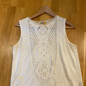 Vit ärmlös topp med spets från Zara - Supersnygg vit ärmlös topp/linne från Zara med detaljerad spets och broderier framtill. Toppen har rund halsringning och ett unikt mönster i spetsen som ger en cool vibe.