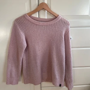 Ljusrosa stickad tröja - Mysig ljusrosa stickad tröja med ribbad struktur och rund hals. Perfekt för kyliga dagar och enkel att matcha med jeans eller kjol. Tröjan har långa ärmar och en avslappnad passform som ger en skön och chill vibe.