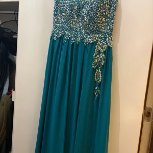 Turkos långklänning med paljetter - Säljer en magisk turkos långklänning från WNSN, täckt med glittriga paljetter upptill och på sidan. Klänningen har en flowy kjol och är axelbandslös, perfekt för bal eller fest. Materialet känns lätt och har ett lyxigt fall. Gör dig redo att glänsa!