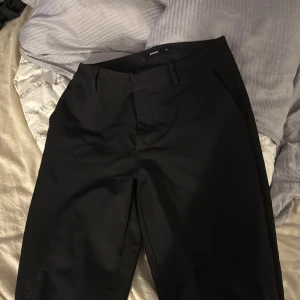 Svarta kostymbyxor från Bik Bok - Svarta kostymbyxor från Bik Bok med klassisk rak passform och hällor för bälte. Byxorna har diskreta sidfickor och stängs med dragkedja och hake. Perfekta för en clean och stilren look.