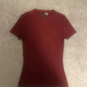 Vinröd t-shirt  - En enkel och snygg vinröd t-shirt från Divided i storlek XS. Modellen är klassisk med rund hals och korta ärmar. Materialet är mjuk bomull som sitter skönt mot kroppen. Perfekt för dig som gillar stilrena och basic plagg i garderoben. En aning nopprig men syns inte väldigt tydligt 
