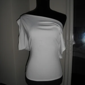 Venderbys - Vit offshoulder topp i stretch - Säljer en vit offshoulder topp med lös passform över axlarna och tightare midja. Tunt och stretchigt material som ger en snygg siluett. Perfekt för dig som gillar en enkel men trendig look.