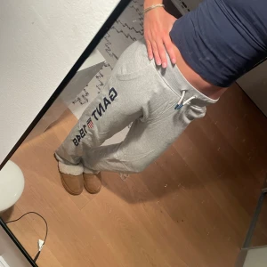 Grå mjukisbyxor - Snygga grå mjukisbyxor från Gant med stort tryck 'GANT 1949' och sköld på benet. Byxorna har dragsko i midjan, ribbad mudd och två fickor. Perfekta för chill dagar eller när du vill vara extra bekväm. Jag är 168cm och dom passar perfekt ti mig!