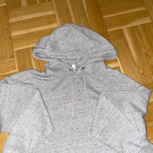 Grå hoodie från H&M - Säljer en gråmelerad hoodie från H&M Divided i storlek S. Tröjan har huva med snörning och långa ärmar.