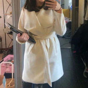 Vit omlottkappa med bälte - Snygg vit kappa med omlottmodell och knytband i midjan.