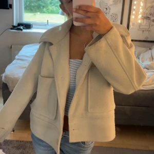 Beige kappa från Kappahl S - Säljer en beige jacka från Kappahl, storlek S. Jackan har stora fickor framtill, bred krage och stängs med knappar. Perfekt för dig som gillar en clean och stilren look med lite boxig passform. skick 8/10 då den är lite smutsig just nu och nopprig.