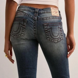 True Religion blå bootcut jeans (fri frakt kolla min profil!!!) - Säljer ett par blå low waist jeans från True Religion med bootcut passform. Jeansen har röda kontrastsömmar. Dom är sydda vid midjan men det går att sprätta bort.  Skriv om ni vill att jag ska ta bort det jag har sytt runt midjan!!! Storlek 28 vilket ungefär motsvaras storlek S/36. Nya pris är 1 299