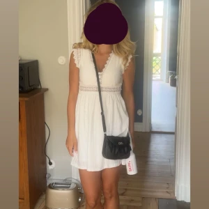 Vit spetsklänning med v-ringning - Säljer en söt vit kortklänning med spetsdetaljer och v-ringad hals. Klänningen har broderade detaljer, korta ärmar med spetskant och ett smockat midjeband som ger en fin siluett. Perfekt för sommarens alla tillfällen!