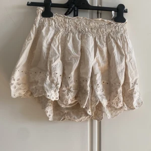 Vita broderade shorts med spetskant från Zara - Supersöta vita shorts med hög midja och bred resår. De har broderade detaljer och spetskant med blommönster längst ner, vilket ger en romantisk och somrig vibe. Perfekta till varma dagar och lätta att matcha med en enkel topp.