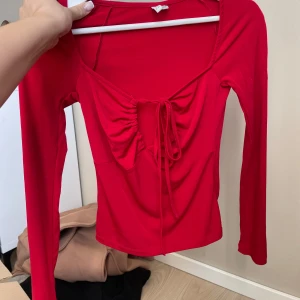 Röd långärmad topp med snörning NLY Trend - Säljer en röd långärmad topp från NLY Trend i storlek XS. Toppen har djup v-ringning med snygg snörningsdetalj framtill och croppad passform. Mjuk och stretchig känsla, perfekt för att sticka ut lite extra.