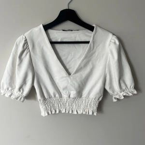 Vit blus från NA-KD - Superfin vit blus från NA-KD med djup v-ringning och puffiga korta ärmar. Storlek S