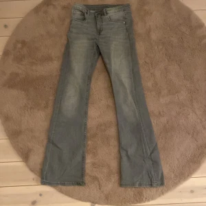 Grå bootcut jeans från Kappahl - Snygga grå jeans från Kappahl i storlek 152. Modellen har klassisk femficksdesign, raka ben med bootcut och subtila slitningar framtill. Jeansen är tillverkade i mjukt bomullsmaterial med lite stretch för extra komfort. Perfekt för dig som gillar en avslappnad och trendig look.
