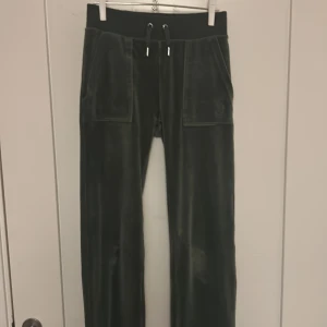 Mörkgröna velourbyxor Juicy Couture XXS - Mörkgröna mjukisbyxor från Juicy Couture i glansig velour. Byxorna har bred resårmidja med snörning, stora fickor fram och bak med knappar samt broderad Juicy Couture-logga. Perfekta för en chill och trendig look.💚😊