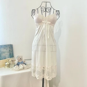 Cremefärgad nattlinne med spetsdetailjer och rosett - Supersöt cremefärgad nattlinne från Japan med tunna axelband och spetsdetaljer vid byst och nederkant. Är ganska genomskinlig på nedre delen. Perfekt för dig som gillar något som är söt och sexig samtidigt. Storlek: XS (32-34). Byst: 75-90cm. Dockans storlek: 34.