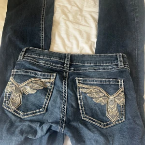Low waist bootcut jeans med broderade bakfickor - Snygga blå jeans från Gina Tricot med kontrastsömmar och unika broderade detaljer på bakfickorna. Säljer eftersom dom börjar bli för korta för mig!🥰 Pris går att diskutera!