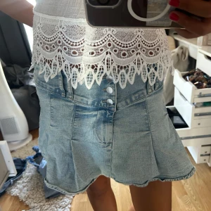 Ljusblå jeanskjol med knappar - Säljer en ljusblå jeanskjol med snygga knappar framtill och lätt utsvängd form. Kjolen har fickor och en cool, casual vibe som passar perfekt till sommarens outfits. Den är kort och har en klassisk jeanslook med mjukt material.