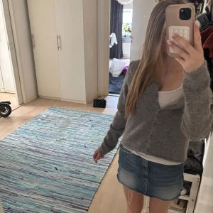 Grå kofta från Gina Tricot - Mysig grå kofta från Gina Tricot med croppad passform och långa ärmar. Koftan har rund halsringning och knäppning framtill med små knappar. Perfekt att slänga över ett linne eller t-shirt för en chill look.