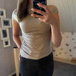 Beige figurnära topp med rynk - Säljer en beige, figurnära topp med korta ärmar och snygg rynkdetalj/dragsko längs ena sidan. Använd högst 2 ggr💗