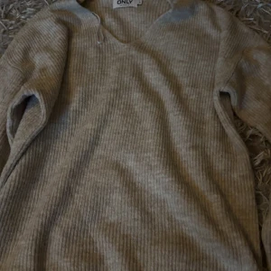 Beige ribbad stickad tröja ONLY - Supermjuk beige stickad tröja från ONLY i ribbat material. Tröjan har v-ringning och långa ärmar, perfekt för lager på lager. Enkel att matcha med jeans eller kjol för en chill look.