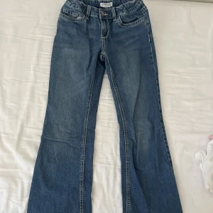 Blå bootcut jeans från Lindex - Snygga blå jeans från Lindex med bootcut passform och klassisk femficksdesign. Jeansen har markerade sömmar och coola bakfickor med lock och knappdetalj. Perfekta för dig som gillar en retroinspirerad look.