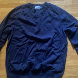 Mörkblå tröja från Calvin Klein Kashmir mix - Snygg mörkblå tröja från Calvin Klein i storlek S. Tröjan har en klassisk rund halsringning med ribbad kant och långa ärmar. Materialet känns mjukt och skönt, perfekt för chill dagar. Enkel och stilren design utan mönster eller detaljer.