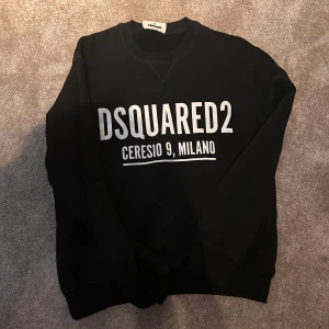 Svart sweatshirt från Dsquared2 - Svart sweatshirt från Dsquared2 med stor vit logotyp och texten 'Ceresio 9, Milano' på bröstet. Tröjan har rund hals, långa ärmar och är tillverkad i mjuk bomull. Perfekt för dig som gillar streetwear och vill sticka ut med ett snyggt designerplagg.
