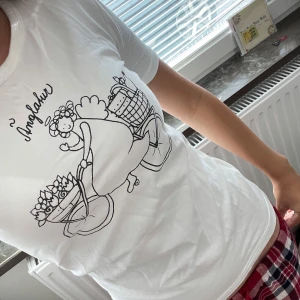 Vit t-shirt med änglamotiv No Problem - Vit t-shirt med ett gulligt svart tryck av en ängel som cyklar med blommor och korgar. Bomull tröja. Storlek S/XS