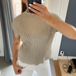 Beige ribbad stickad topp - Snygg beige ribbad stickad topp med korta ärmar och högre rund hals. I storlek XS men passar en S också. 