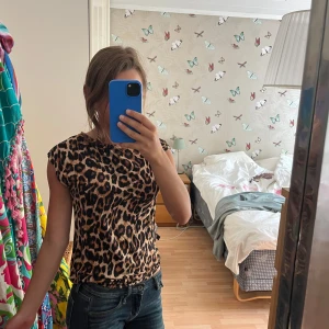 Leopardmönstrad topp i stretchigt tyg - Säljer en snygg leopardmönstrad topp med korta ärmar och rak hals som är på gränsen till en halv polo i storlek S. Sitter som en smäck. Toppens material är mjukt och stretchigt väldigt luftigt och skön som en mjukis tröja på kvällen och perfekt på dagen. vilket gör den bekväm att bära hela tiden. Färgerna går i beige, brunt och svart. Perfekt för dig som vill sticka ut med ett djurmönster.