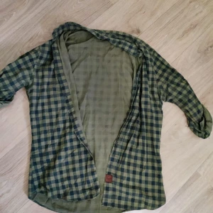 Grönrutig overshirt i bomull - Snygg overshirt i grönt och mörkblått rutigt mönster. Skjortan har lång ärm och är tillverkad i mjuk bomull, perfekt att slänga över en t-shirt. Avslappnad passform och klassisk krage.