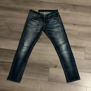 Mörkblå jeans med slitningar - Snygga mörkblå jeans av märket dondup med slitningar och tydliga kontrastsömmar. Jeansen har klassisk femficksdesign, orange detaljer på bakfickorna och en cool tvättad look. Perfekta för dig som gillar en avslappnad men trendig stil.