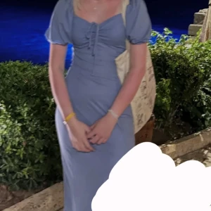 Blå långklänning med puffärm - Supersöt långklänning i blått med puffärmar och snörning framtill. Klänningen har en smickrande v-ringning och är figurnära upptill med en lätt utställd kjol. Perfekt för sommarkvällar och har en romantisk vibe.