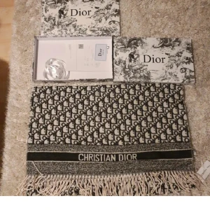 Svartvit halsduk från Christian Dior - Exklusiv halsduk från Christian Dior med ikoniskt monogrammönster i svart och vitt. Tjockt material med fransar i kanterna och tydlig logga. Perfekt accessoar för att lyfta din outfit med lyxig vibe.