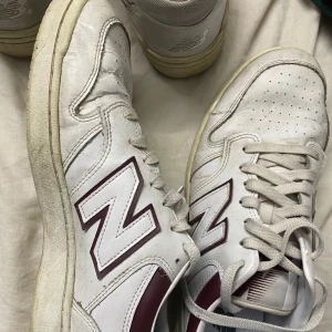 Vita New Balance sneakers med vinröda detaljer 47storlek - Snygga vita New Balance sneakers med vinröda detaljer och klassisk N-logga på sidorna. Skorna har snörning, perforerad tå och platt sula. Tillverkade i skinn och syntet, perfekta för en clean och sportig stil.