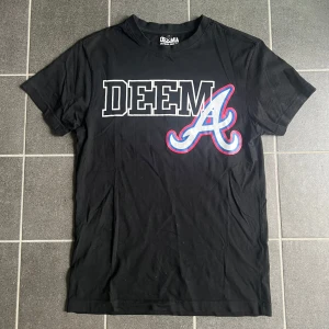 2kdeema tshirt  - Svart t-shirt från 2kdeema med stort vitt och rött tryck framtill. Klassisk rund hals och korta ärmar. T-shirten är i mjuk bomull och har en sportig vibe med tydlig logga och grafisk design över bröstet.