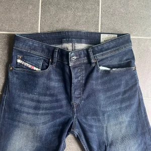 Mörkblå Diesel jeans  - Säljer ett par mörkblå Diesel jeans med klassisk femficksdesign och snygga slitningar framtill. Jeansen har raka ben och normal passform, med läderpatch bak i midjan och diskreta kontrastsömmar. 