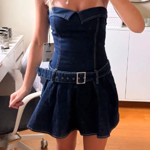 Mörkblå jeansklänning Bershka - Supersnygg mörkblå jeansklänning med bälte. Axelbandslös modell och superfin passform. Ny med prislapp kvar. Storlek small på lappen men väldigt liten i storlek så passar någon med xs. Buda gärna 💓