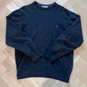 Mörkgrå burberry tröja av lammull - Snygg mörkgrå stickad tröja från Thomas Burberry med diskret broderad logga på bröstet. Klassisk rund halsringning och ribbade muddar. Perfekt för dig som gillar stilrena och tidlösa plagg.                                                Storlek är i S men kan även fungera som en större XS. Kan förekomma att den är lite hårig och har lite knop längs underarmarna men i övrigt bra kondition utan defekter. Pris kan diskuteras.