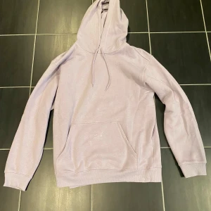 Ljuslila hoodie med huva och ficka - Säljer en stilren ljuslila hoodie med huva och dragsko. Tröjan har en stor magficka och ribbade muddar vid ärmslut och nederkant. Perfekt för chill dagar eller när du vill ha en enkel men snygg look. Från HM och i mycket fint skick!