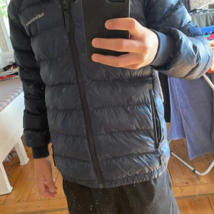 Mörkblå Peak Performance dunjacka - Säljer en mörkblå dunjacka från Peak Performance. Den har ett super litet hållpunkt luvan som ni ser på bild 3 och på armen har jag sytt för ett hål. Storlek 160