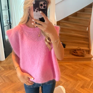 Ljusrosa stickad ärmlös tröja - Superfin ljusrosa stickad tröja i oversize-modell. Tröjan är ärmlös med breda axlar och har en rund halsringning. Perfekt att styla över en skjorta eller t-shirt för en trendig look.