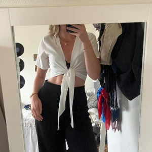 Vit omlottopp med knytdetalj  - Säljer en fräsch vit omlottopp/blus. Toppen är croppad med korta, vida ärmar och har en snygg knytning framtill. Knytningen gör att man kan styla på flera olika sätt, se bilderna. Tjockare material framtill men lite mer see through bak. 