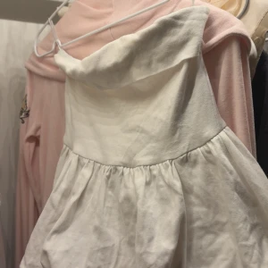 Vit axelbandslös kortklänning - Supersöt vit blus med axelbandslös design och voluminös kjol. Perfekt för dig som vill ha en enkel men stilren look. blusen har en lätt rynkad midja och är gjord i ett mjukt bomullstyg. Används aldrig .