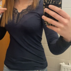Mörkblå långärmad spetsblus - Supersnygg mörkblå långärmad topp med v-ringning och spetsdetaljer längs halsringningen. Sitter tight och har en feminin look, säljer för att den inte används och vill köpa en likadan i svart! Köptes för 559 och använd ca 5 gnr. Har dock ett litet hål längst ner, den är mindre än en lillfinger nagel typ. Der är bara att be om fler bilder❤️