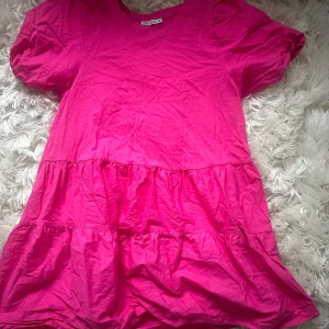Rosa kort klänning från Zara - Supersöt rosa kortklänning från Zara med puffärmar och volangdetaljer. Tillverkad i mjuk bomull, perfekt för sommarens alla tillfällen. Enkel och trendig design som är lätt att styla med sneakers eller sandaler. Tar frakt!