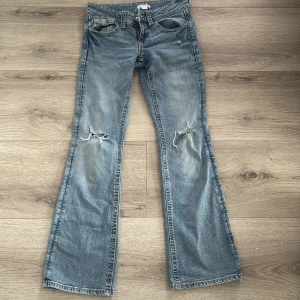 Blå bootcut jeans från Gina Tricot - Snygga ljusblå bootcut jeans från Gina Tricot med slitna detaljer på knäna och coola fickor med lock och knapp. Klassisk femficksmodell i mjuk bomullsdenim, perfekt för dig som gillar en avslappnad och trendig look.